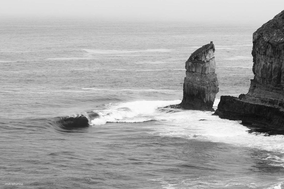 Lone sea stack rising from the Southern Ocean - Eyre Peninsula South Australia rugged coastline near Cummings Monument - black and white fine art coastal landscape photography - wave breaking at cliff base - Josh Whiting