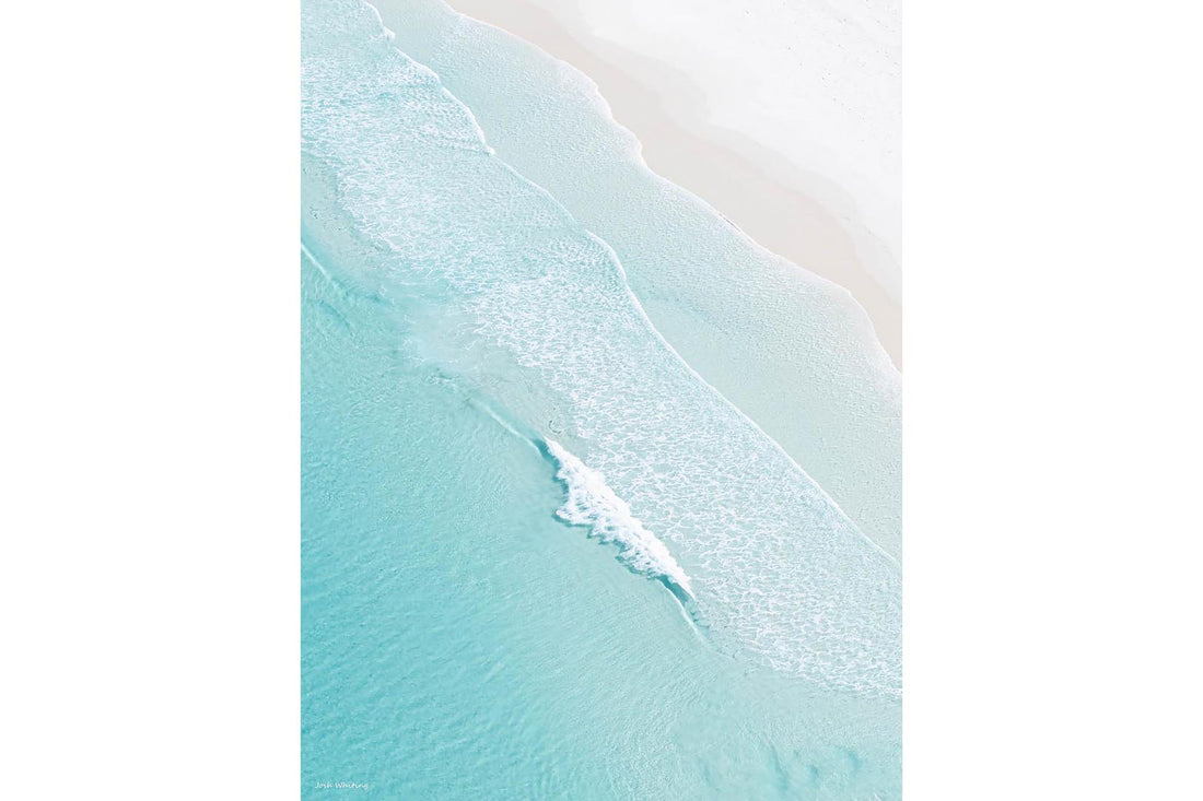 Aerial photograph of the Australian coastline — turquoise water meeting pale sand in a sweeping diagonal line, part of Josh Whiting's coastal wall art series