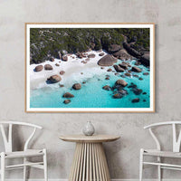 Oak framed print of granite boulders and turquoise water, a warm toned piece of Australian beach wall art